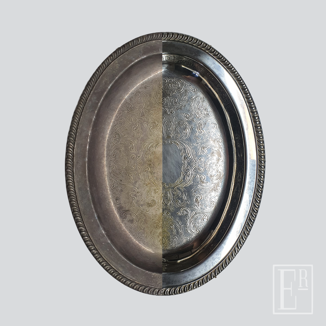 An engraved silver serving tray, shown half tarnished and half re-polished